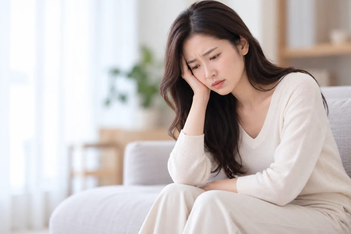 창가 소파에 앉아 걱정스러운 표정으로 고민하는 여성